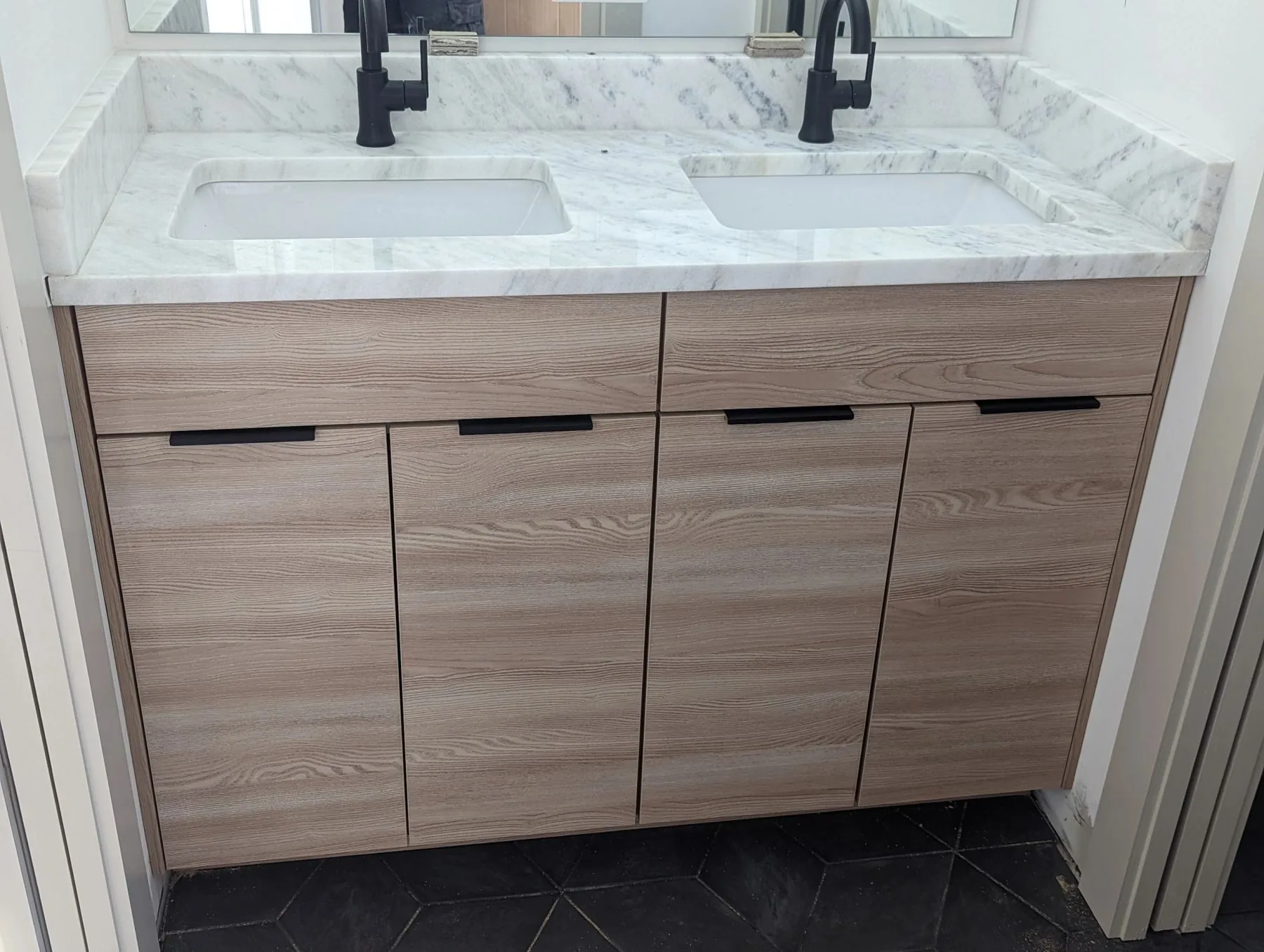 A double vanity in light oak with marble counters and black fixtures